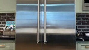 Un frigorifero in acciaio inox con doppie ante in una cucina con mobili color verde chiaro e uno schienale in mattoni.