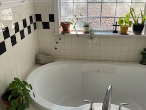 A bathroom with a bathtub, white tiled walls, a window with potted plants, and a stone on the floor. - Stylish Family Home: Walk to Downtown Commerce 10 guests: 5BR/4BA (Commerce)