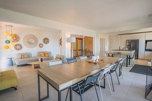 A modern kitchen with a central island, a dining area with a long table and chairs, and a living space with a sofa and decorative wall art. - Villa in Carqueiranne. Beautiful sea views, 5 bedrooms, heated swimming pool. (Carqueiranne)