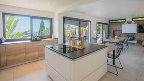 A modern kitchen with a central island, large windows, and a stone fireplace. - Villa in Carqueiranne. Beautiful sea views, 5 bedrooms, heated swimming pool. (Carqueiranne)