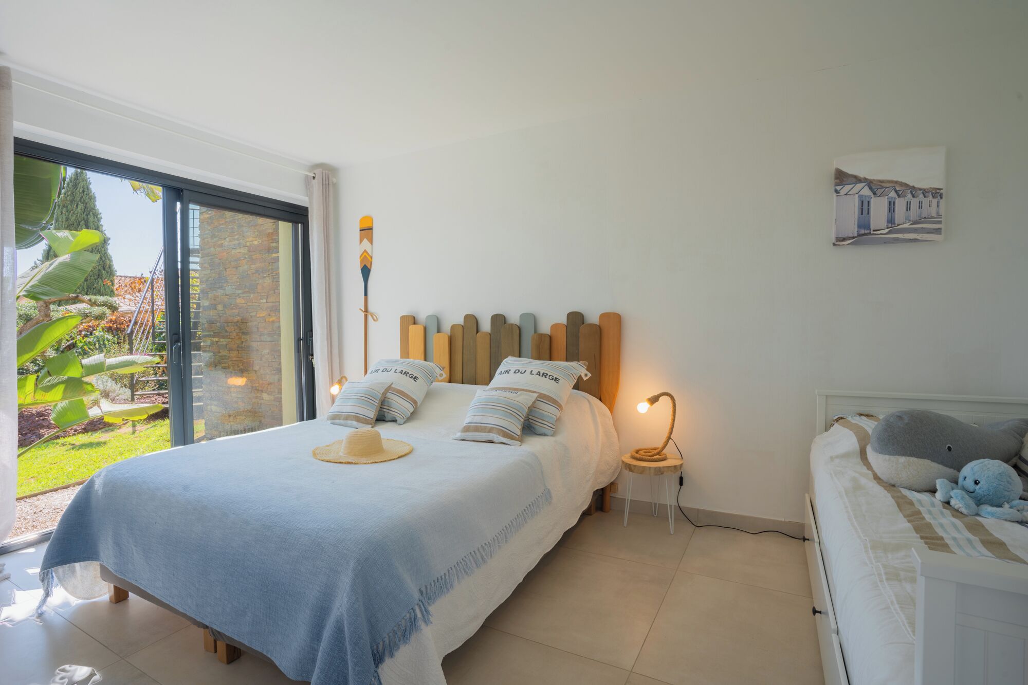 A bedroom with a bed, a bedside table, a lamp, a window, and a view of the outdoors.