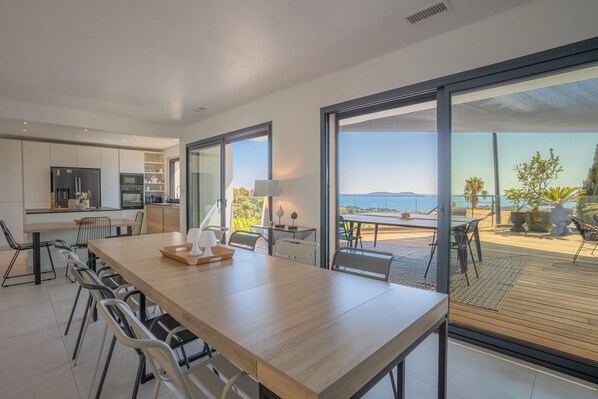 A modern kitchen with a dining area and a large sliding glass door leading to a deck with a view of the sea. - Villa in Carqueiranne. Beautiful sea views, 5 bedrooms, heated swimming pool. (Carqueiranne)