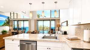 A modern kitchen with a dishwasher, a large island with a sink, and a view of the ocean. - Napili Point | Oceanfront 2 BR | Water Front | Car Incl. w/ 6+ Nights | NAP-C19 by KBM (Lahaina)