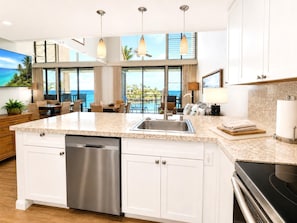 Una cocina moderna con lavavajillas, una isla grande con pileta y vista al océano.