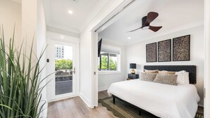 Une chambre à coucher avec un lit, un ventilateur de plafond, une table de chevet, une lampe et une vue sur l’extérieur.