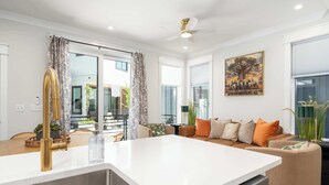 Une cuisine moderne avec un plan de travail blanc, un robinet doré et un coin repas comprenant une table et des chaises en bois.