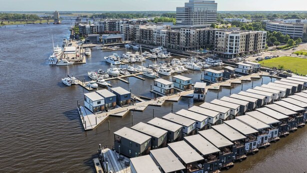 A marina with boats docked, a large building with multiple floors, and a grassy area.