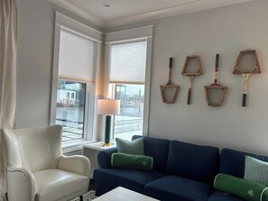 Ein Zimmer mit einem weißen Sessel, einem blauen Sofa und einer Lampe auf einem kleinen Tisch. Vier Rackets sind an der Wand befestigt.