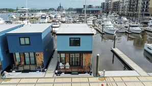 Un port de plaisance avec des bateaux amarrés, un bâtiment doté d’une terrasse et de chaises, et une voie navigable.