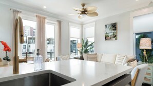Une cuisine moderne dotée d’un îlot central, d’un ventilateur de plafond et offrant une vue sur le paysage urbain grâce à de grandes fenêtres.