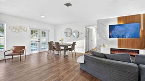 A modern living room with a dining area, a flat-screen TV, and a fireplace. - Fun Miami Pool Home  Pickable, Firepit, Pingpong (Miami)
