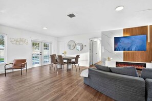 A modern living room with a dining area, a flat-screen TV, and a fireplace. - Fun Miami Pool Home  Pickable, Firepit, Pingpong (Miami)