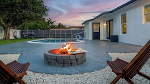 A backyard with a swimming pool, a fire pit, and two wooden chairs. - Fun Miami Pool Home  Pickable, Firepit, Pingpong (Miami)