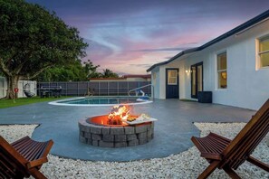 A backyard with a swimming pool, a fire pit, and two wooden chairs. - Fun Miami Pool Home  Pickable, Firepit, Pingpong (Miami)