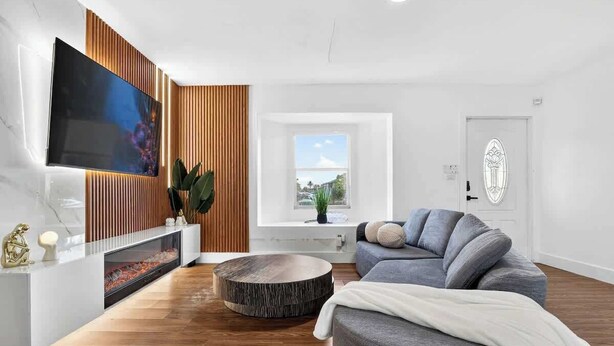 A modern living room with a flat-screen TV, a round wooden coffee table, a grey sofa, and a window with a view. - Fun Miami Pool Home  Pickable, Firepit, Pingpong (Miami)