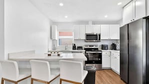 A modern kitchen with white cabinets, a stainless steel refrigerator, and a central island with bar stools. - Fun Miami Pool Home  Pickable, Firepit, Pingpong (Miami)