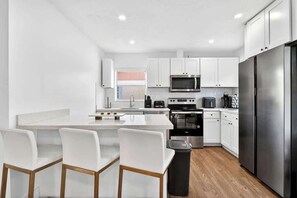 A modern kitchen with white cabinets, a stainless steel refrigerator, and a central island with bar stools. - Fun Miami Pool Home  Pickable, Firepit, Pingpong (Miami)