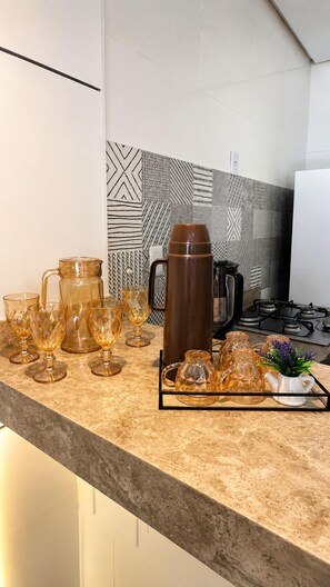 A kitchen counter with a coffee maker, glass cups, and a tray of teapots. - Fully Furnished Duplex Apartment in Porto Seguro - Swimming Pool - 200m from the Beach (Porto Seguro)