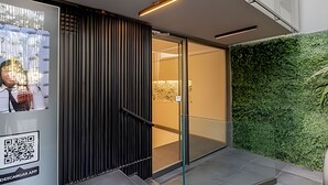 En moderne bygningseingang med glasse, et lodret træpanel og en grøn væg.
