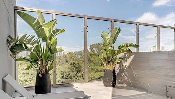 En moderne balkon med store vinduer, plantekrukker og et minimalistisk siddeområde.