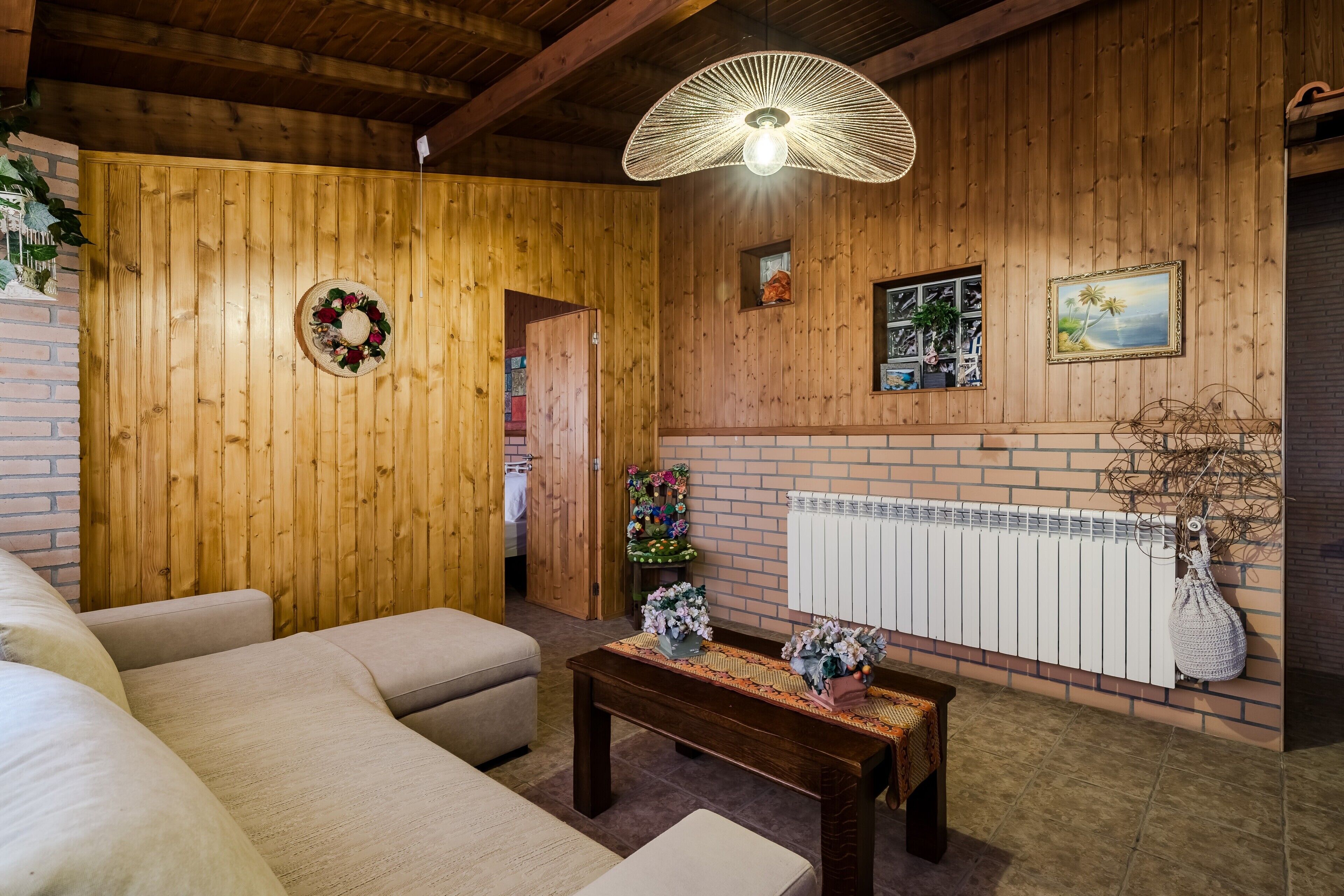 A wooden interior with a sofa, a table with flowers, a radiator, and a hanging light fixture.