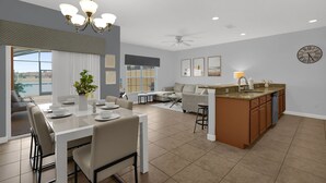 Uma cozinha moderna com uma ilha central, uma sala de jantar com uma mesa e cadeiras brancas, e uma sala de estar com sofá e mesa de centro.