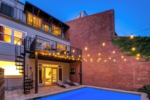 Una casa de dos pisos con piscina, mobiliario exterior e iluminación colgante.