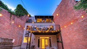 A two-story building with a balcony, a pool, and string lights. - Kirby Poolhouse - Game Room - Garage - Elevator (Houston)