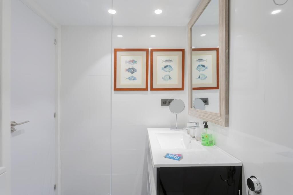 Un baño con un lavamanos blanco, un espejo, cuadros con peces enmarcados y una puerta.