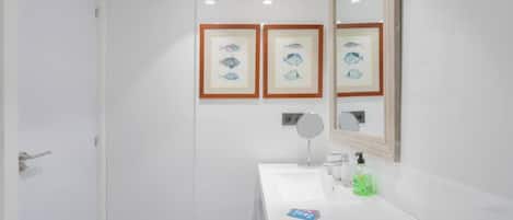 A bathroom with a white sink, a mirror, framed fish pictures, and a door.