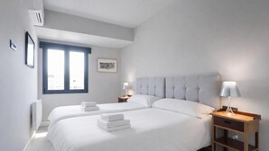 Habitación de hotel con dos camas, una ventana, una mesita de noche con lámpara y aire acondicionado instalado en la pared.