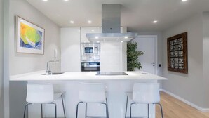Una cocina moderna con una isla central, taburetes de bar, horno empotrado y extractor de acero inoxidable.