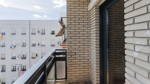 Un balcón con pared de ladrillo, una ventana y barandilla de metal.