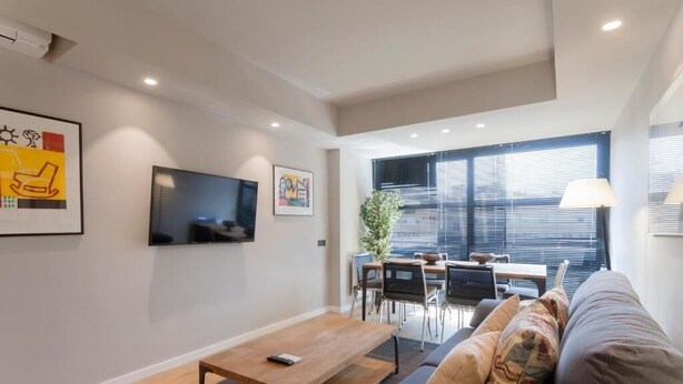 Una sala de estar moderna con un sofá, una mesa de centro, un televisor y un comedor con una mesa y sillas.