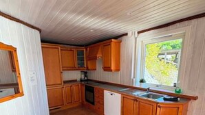 Eine kompakte Küche mit Holzausstattung, einem integrierten Geschirrspüler und einem Fenster mit Blick auf Grünflächen.