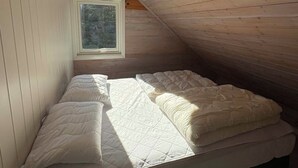 Ein kleiner Raum mit schrägem Dach, einem Bett und einem Fenster.