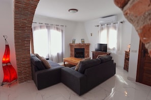 A living room with a sectional sofa, a fireplace, a television, and a brick column. - R1360 Pueblo Alhama 54 (Nerja)