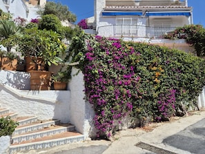 A white building with a staircase and a wall covered in purple flowers. - R1360 Pueblo Alhama 54 (Nerja)