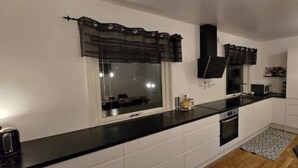 A kitchen with white cabinets, a black countertop, a window with black curtains, a stove, and a microwave. - Villa Apartment in the best part of Gothenburg (Gothenburg)