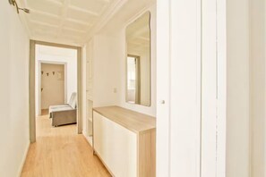 Ein schmaler Flur mit Holzboden, einer hellen Bank und einem Spiegel an der Wand.