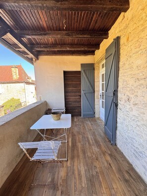 Ein Balkon mit Holzboden, einem weißen Tisch mit Schüssel und einem Metallklappstuhl.