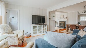 Una sala de estar con televisor, sofá y sillón, un comedor con mesa y sillas, y una chimenea.