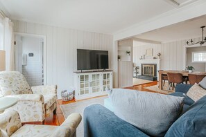 A living room with a TV, sofa, and armchair, a dining area with a table and chairs, and a fireplace.