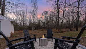 Un patio con sillas Adirondack, una fogata y piso de grava.