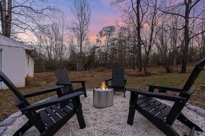A patio with Adirondack chairs, a fire pit, and a gravel ground.