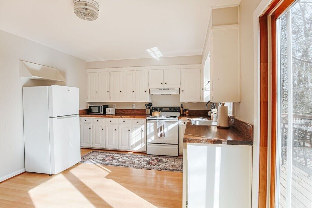 A kitchen with white cabinets, a stove, a microwave, and a refrigerator.