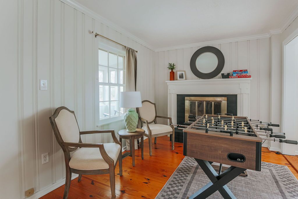 Una habitación con mesa de fútbol, dos sillas, chimenea y ventana con cortinas.