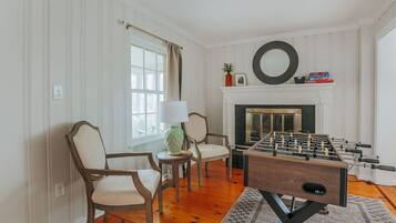 Una habitación con mesa de fútbol, dos sillas, chimenea y ventana con cortinas.