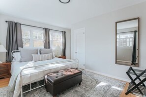 A bedroom with a bed, bedside tables, a mirror, a window with curtains, and a patterned rug.