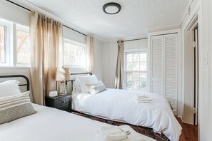 Une chambre avec deux lits, une table de chevet, une lampe et une fenêtre avec des rideaux.